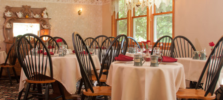 Breakfast room with ivory table cloths, burgundy napkins, sage green mugs, black & oak Windsor chairs, hutch with teapots in background