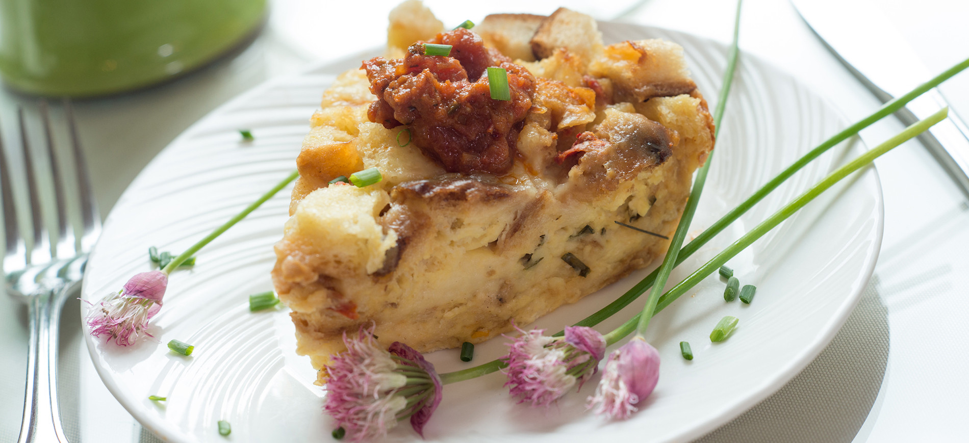 Chive and cheddar strata on white plate with chive blossom garnish