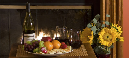 wine bottle, fruit & cheese plate, two glasses wine, sunflowers with fireplace behind