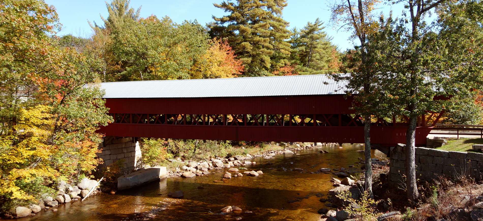 Covered Bridge in NH over river with foliage around it