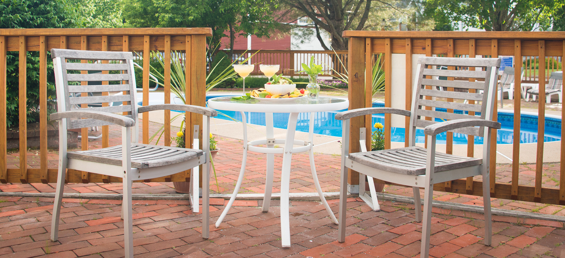 patio with two chairs & table with drinks, fence and pool behind