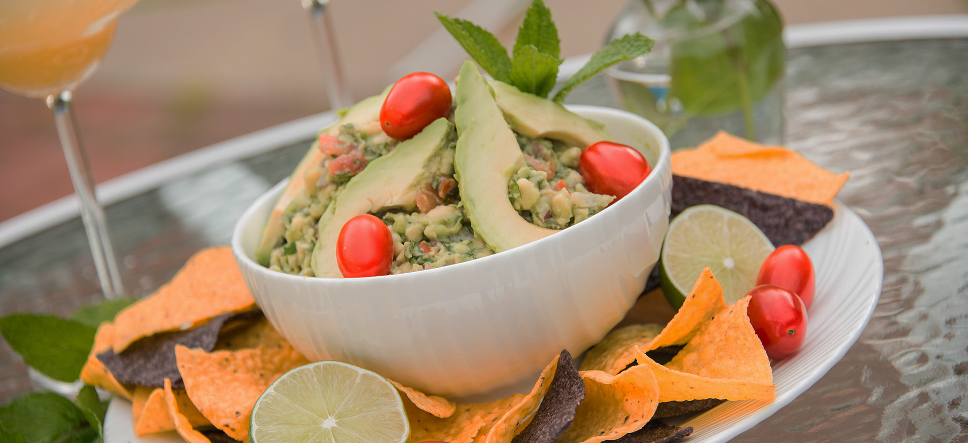 Guacamole with cherry tomato garnish in white bowl surrounded by yellow and blue corn chips