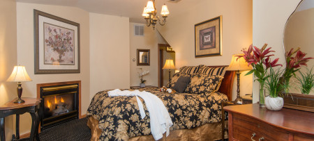 Fireplace with picture above, queen bed with gold & black bedding & white robe below chandelier