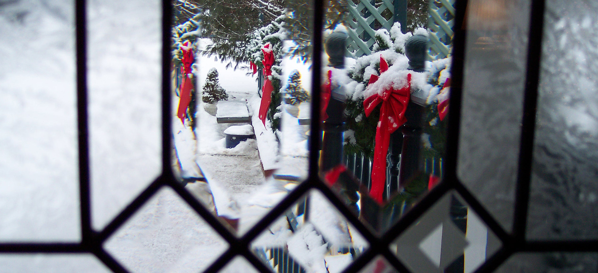 Clear stained glass with view of evergreen roping & red bows in snow outside