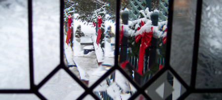 Clear stained glass with view of evergreen roping & red bows in snow outside