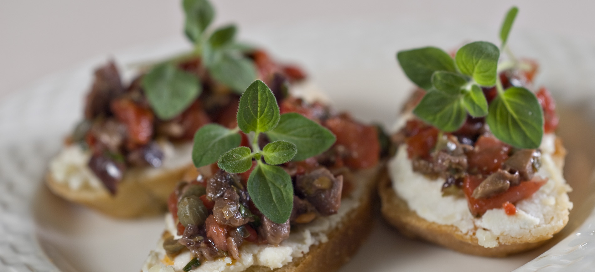 Three pieces of bruschetta topped with tomatoes, olives, oregano