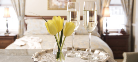 Silver tray with three yellow tulips in vase, two glasses of champagne with bed behind