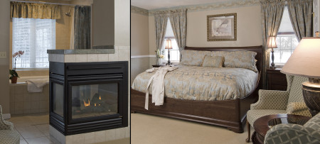 wing chair, jetted tub tub with window above behind three sided gas fireplace, king bed with blue & beige bedding,windows with drapes & nightstand with lamp on each side of bed