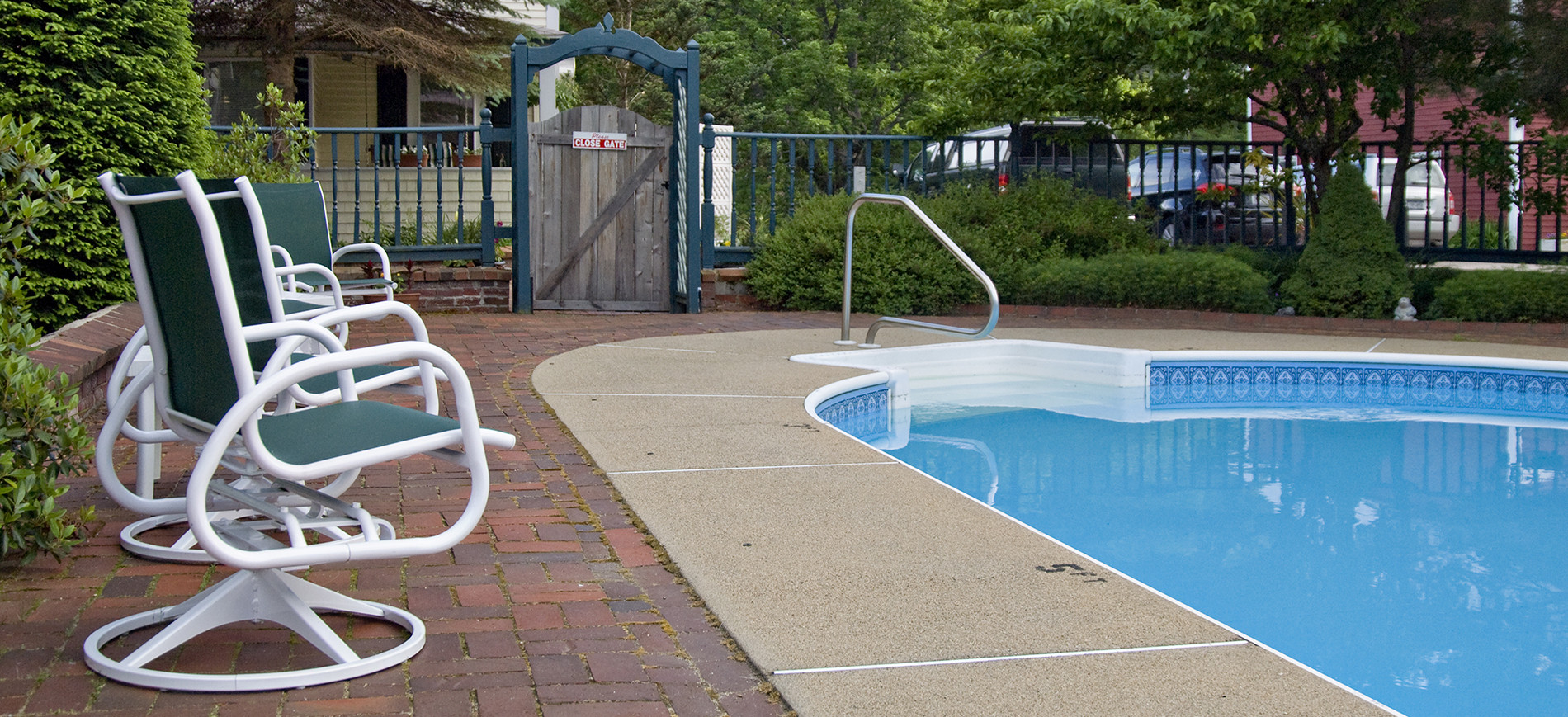 rocking chairs on patio next to pool with fence in background