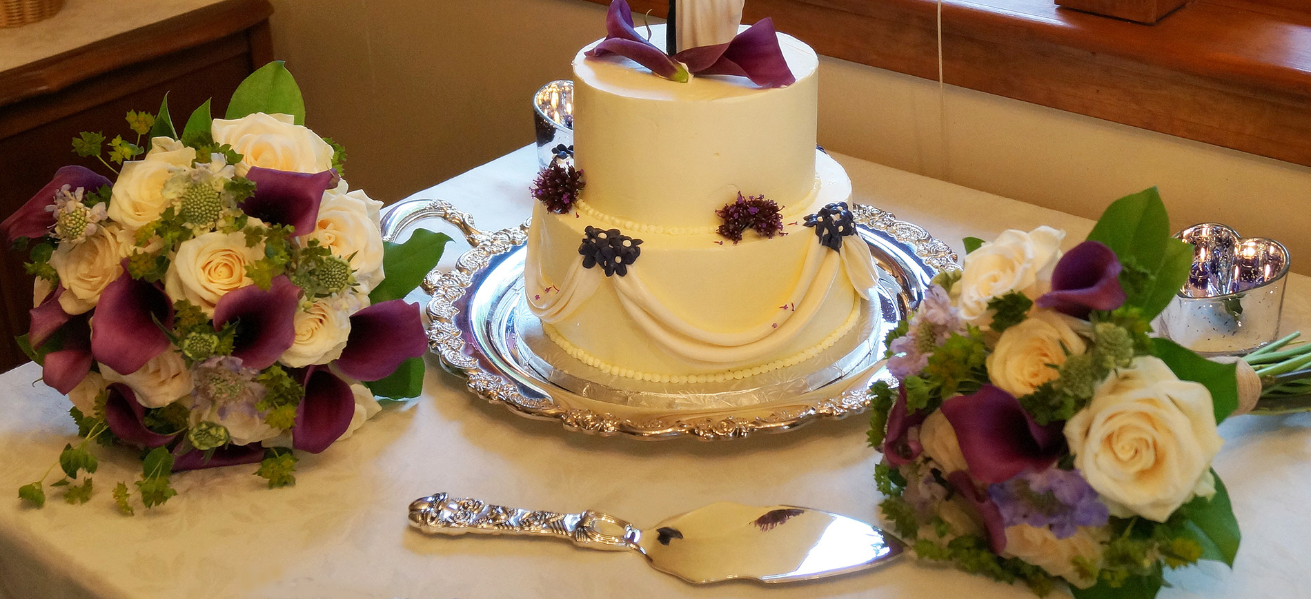 Two tiered wedding cake with bouquets on each side and sliver server in front