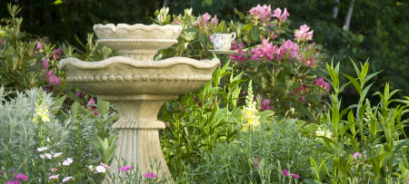 Garden of spring flowers with limestone colored two level fountain on pedestal