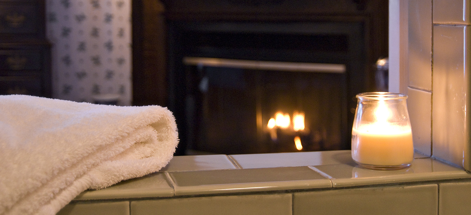 folded towel and candle on jetted tub with fireplace behind