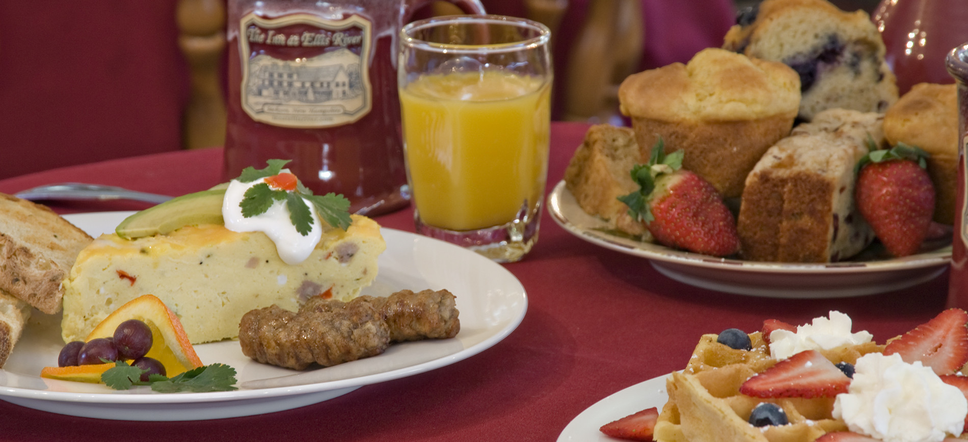 Frittat with sausage & toast on left, mug & orange juice glass, muffins, waffle with strawberry & whipped cream