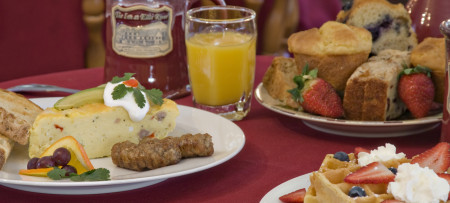 Frittat with sausage & toast on left, mug & orange juice glass, muffins, waffle with strawberry & whipped cream