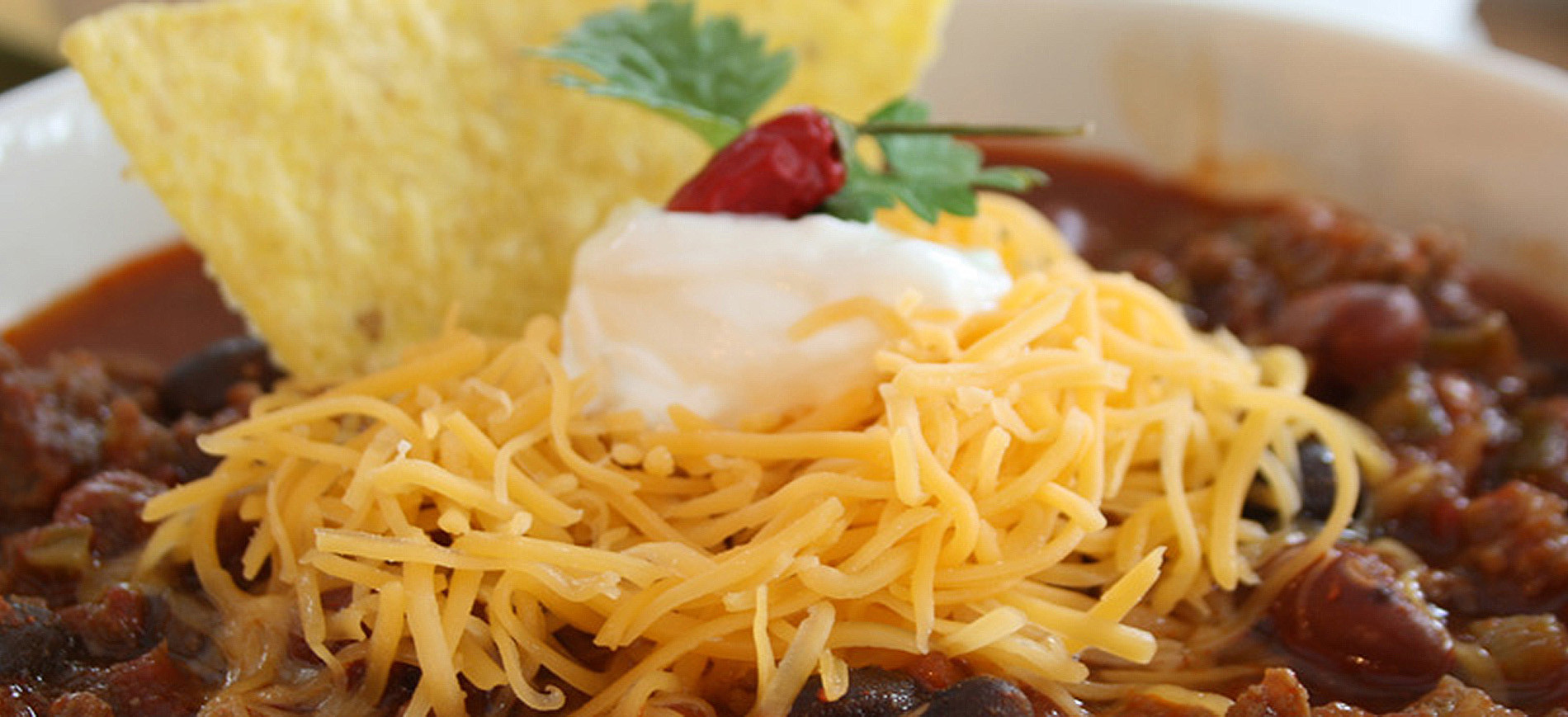 grated cheese, sour cream, cilantro, chili pepper topping on bowl of chili