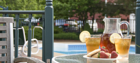 glass topped table with two glasses iced tea with lemon circle garnish & cookies & strawberries on plate, pool in background