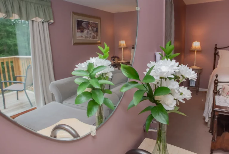 Window nook with white lilies in vase, green plant, and soft wall sconce lighting.
