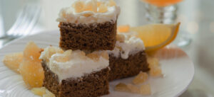 Three stacked pieces of gingerbread with lemon frosting in front of glass mug of cider
