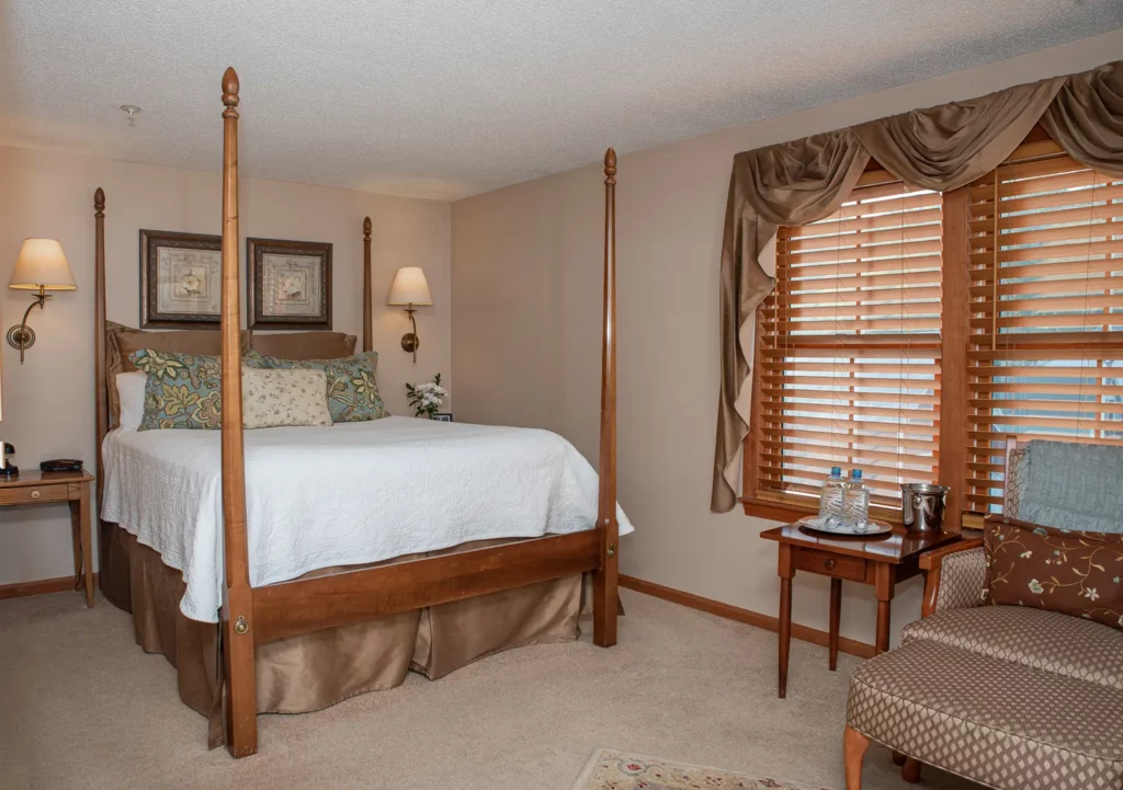 Bedroom with wooden four-poster bed and window seat.