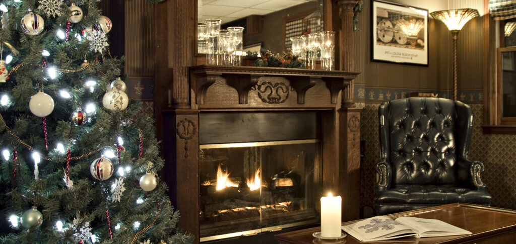 Xmas tree on left, fireplace with mantel, wing chair, coffee table with candle and open book