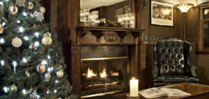 Xmas tree on left, fireplace with mantel, wing chair, coffee table with candle and open book