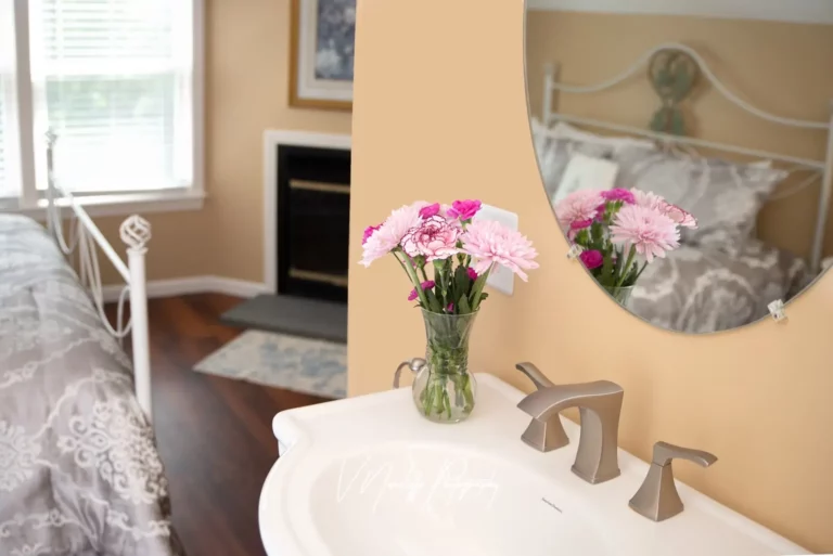 A well-lit bathroom with a sink, mirror reflecting pink flowers.