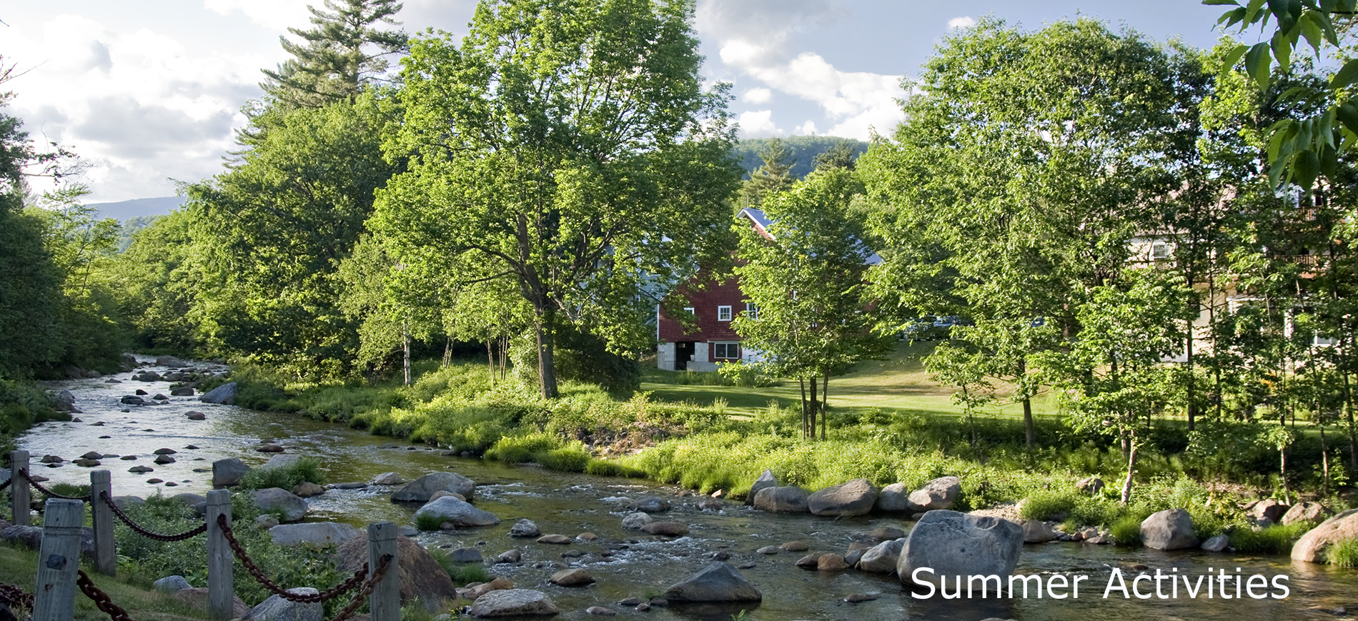 view of Inn at Ellis River across river in summer.