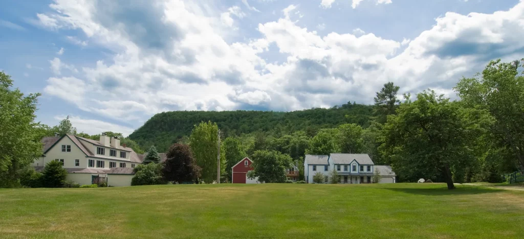 Landscape with houses, red barn, and green hills under a cloudy sky.