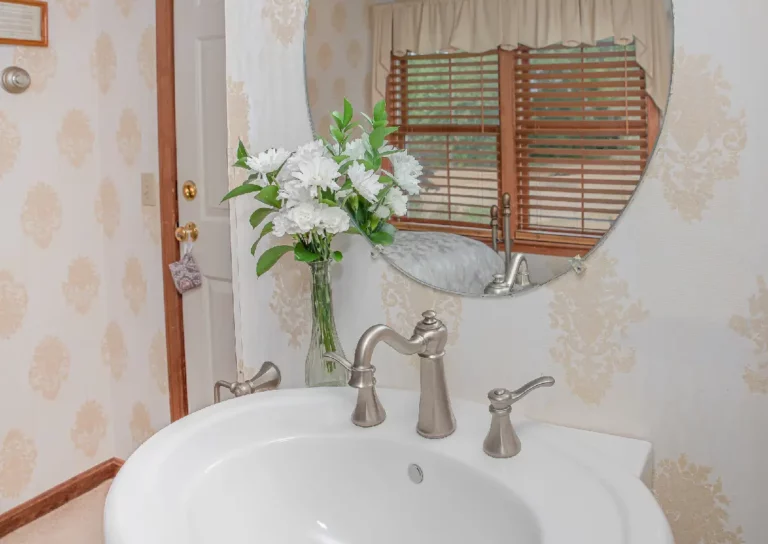 Bathroom vanity with a sink, faucet, mirror, and a vase of white flowers.